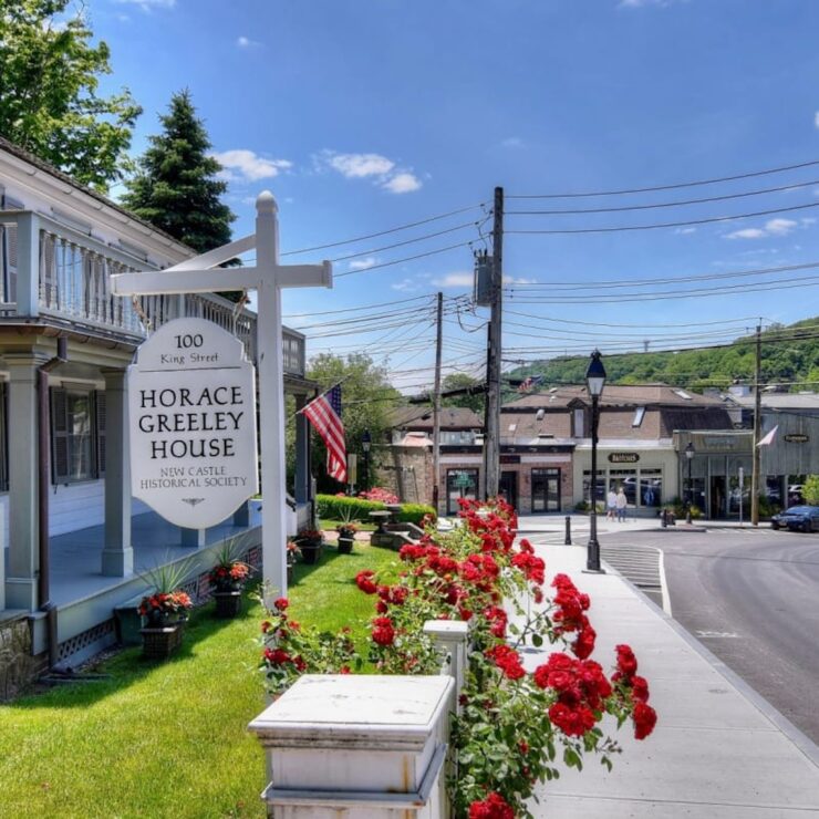 Historic Horace Greeley House and sign on King Street in downtown Chappaqua, NY, with shops and flowers nearby.