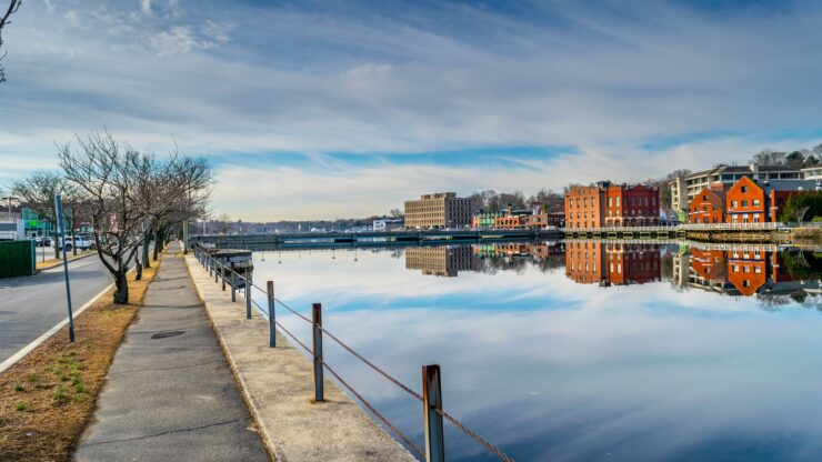 Calm riverfront view in downtown Westport, CT with red brick buildings reflected in the water and a quiet pedestrian path.