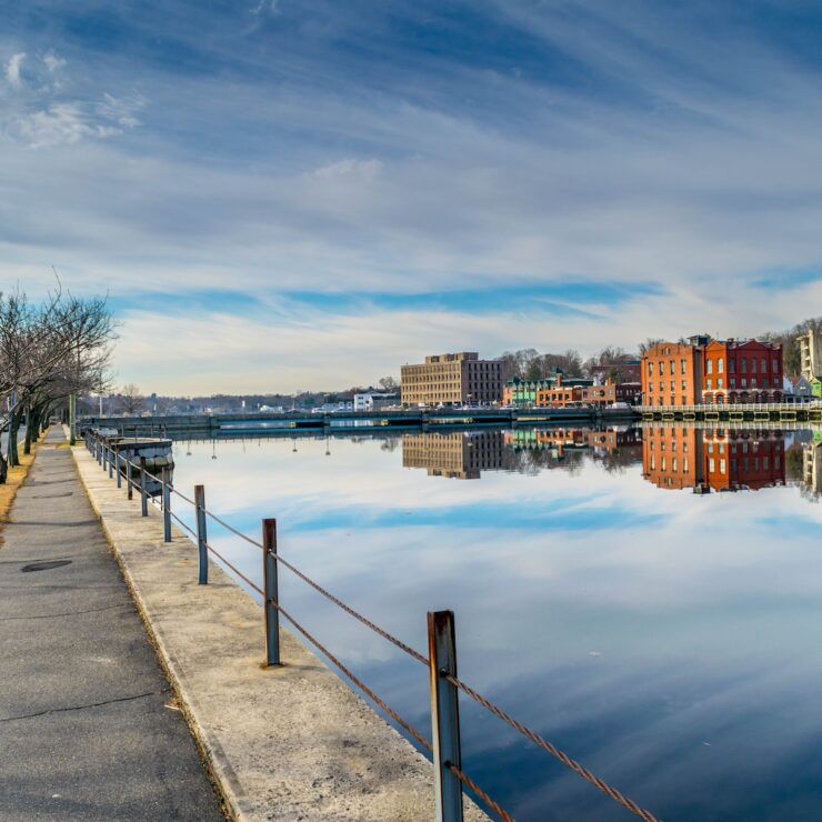 Calm riverfront view in downtown Westport, CT with red brick buildings reflected in the water and a quiet pedestrian path.