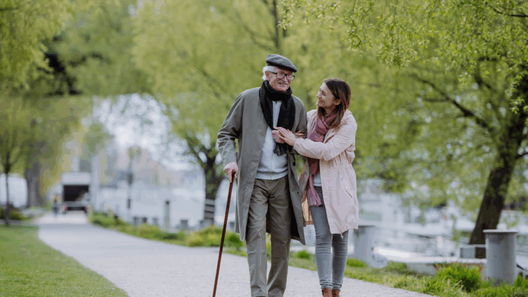 Elderly man in gray coat with gray hat and cane, walking arm-in-arm with younger woman in pink coat.