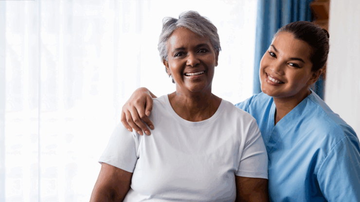 Two smiling women, one older in a white shirt and one younger in blue scrubs.
