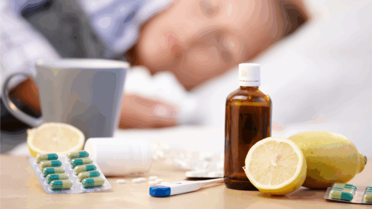 A woman sleeps in bed, surrounded by cold remedies on a table: pills, a thermometer, and a lemon.