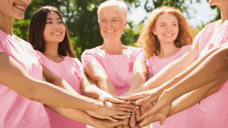 A diverse group of smiling individuals in pink shirts, symbolizing breast cancer awareness.