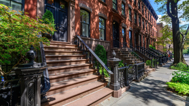 Sunlit row of classic brownstone townhouses with stoops and wrought iron railings in Lower Manhattan.