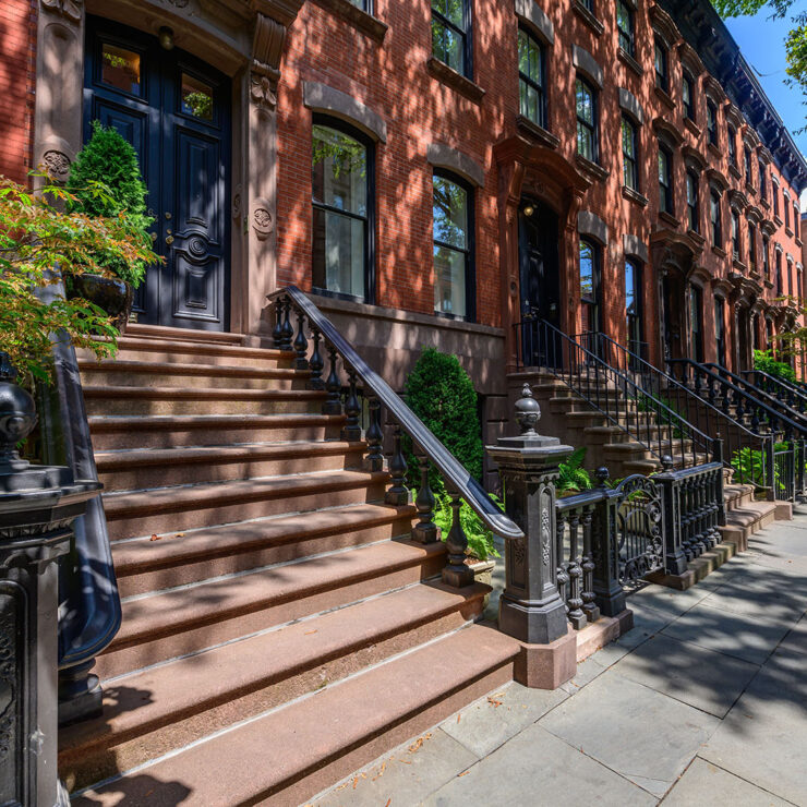 Sunlit row of classic brownstone townhouses with stoops and wrought iron railings in Lower Manhattan.