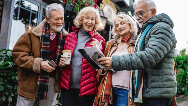 Four cheerful older adults in winter clothes gather outdoors, smiling and looking at a map.