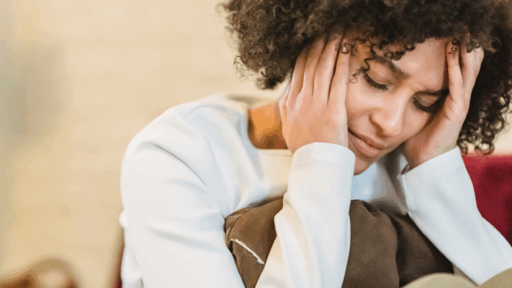 A person with curly hair looks distressed, holding their head in their hands.