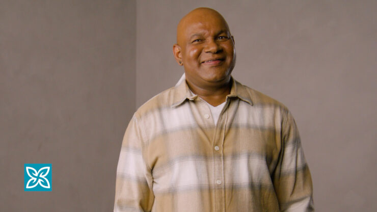 A smiling man is wearing a plaid shirt against a plain background.