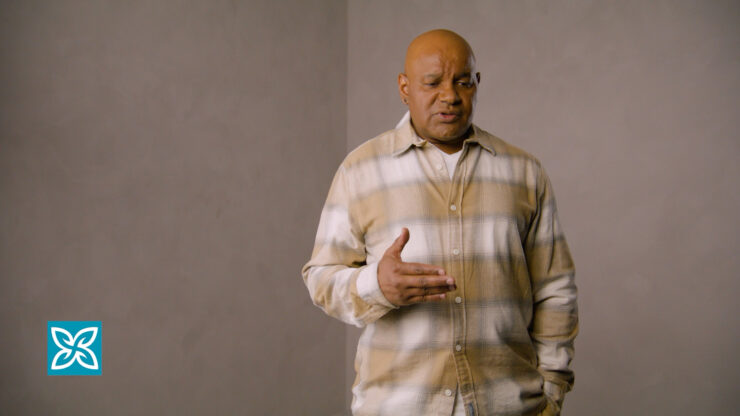 A man is speaking and wearing a plaid shirt against a plain background.