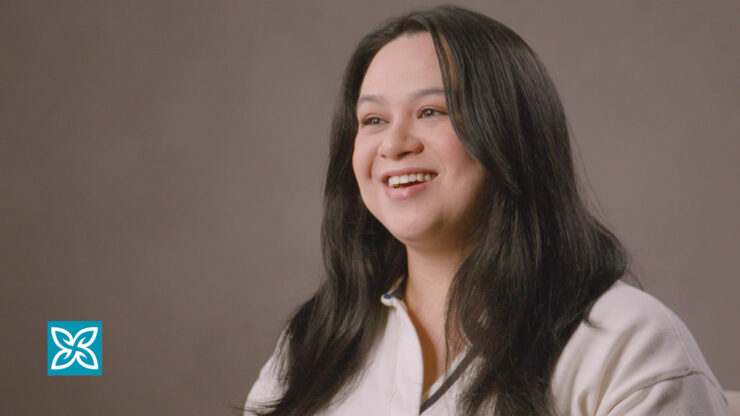 Smiling woman with long dark hair wearing a white top against a neutral background.