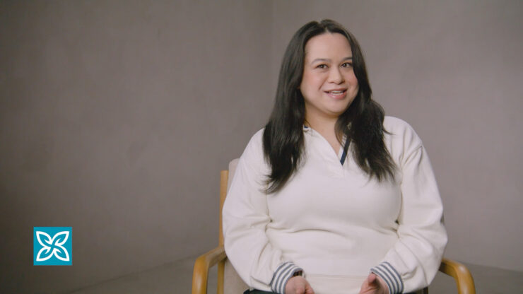 Smiling woman with long dark hair wearing a white top against a neutral background.