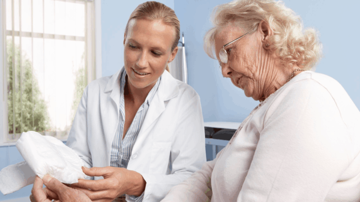A healthcare professional shows an elderly woman an incontinence product in a doctor's office.
