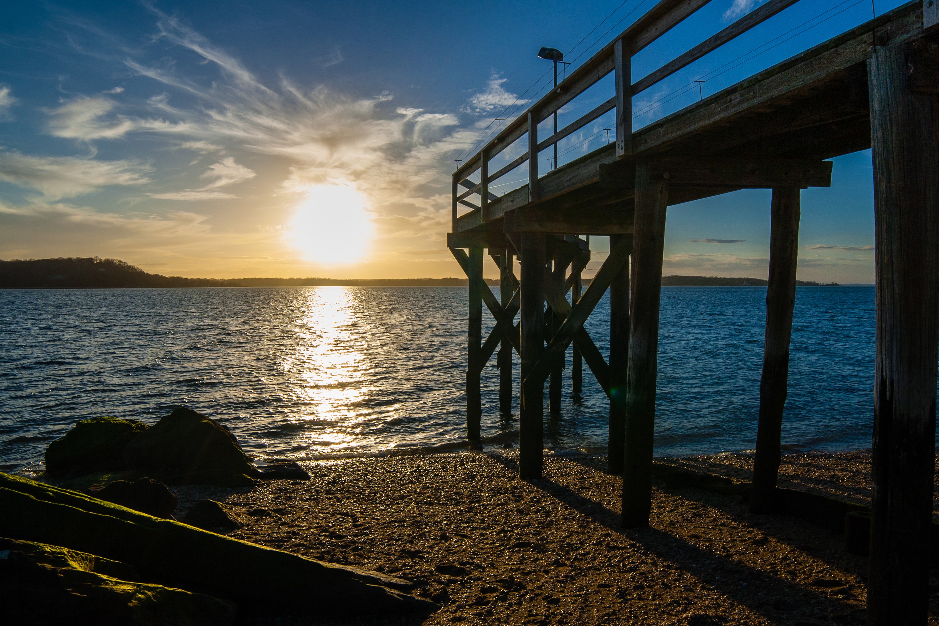 Sunset on West Neck Beach in Huntington, NY showing a wooden pier, reflecting sunlight on the water.