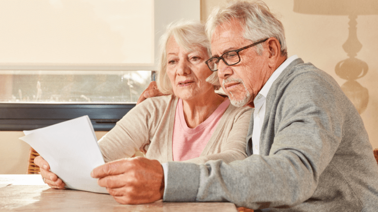 Elderly couple reading a document together at a table, with a serious and focused expression.