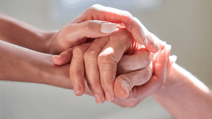 Two hands gently holding an elderly hand, conveying care and compassion.