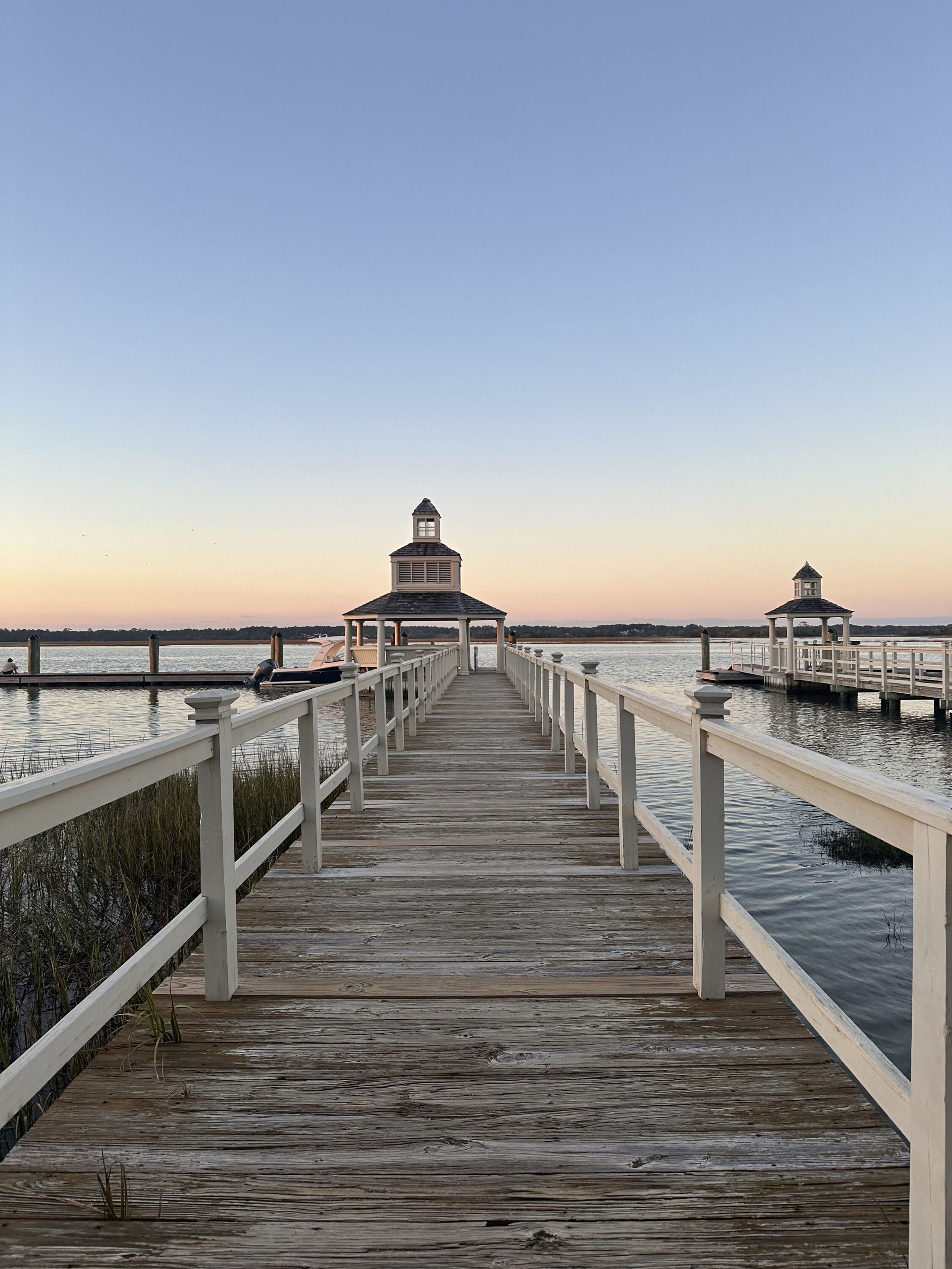 A boardwalk leading to a gazebo over water at sunset, with calm waters and clear sky.