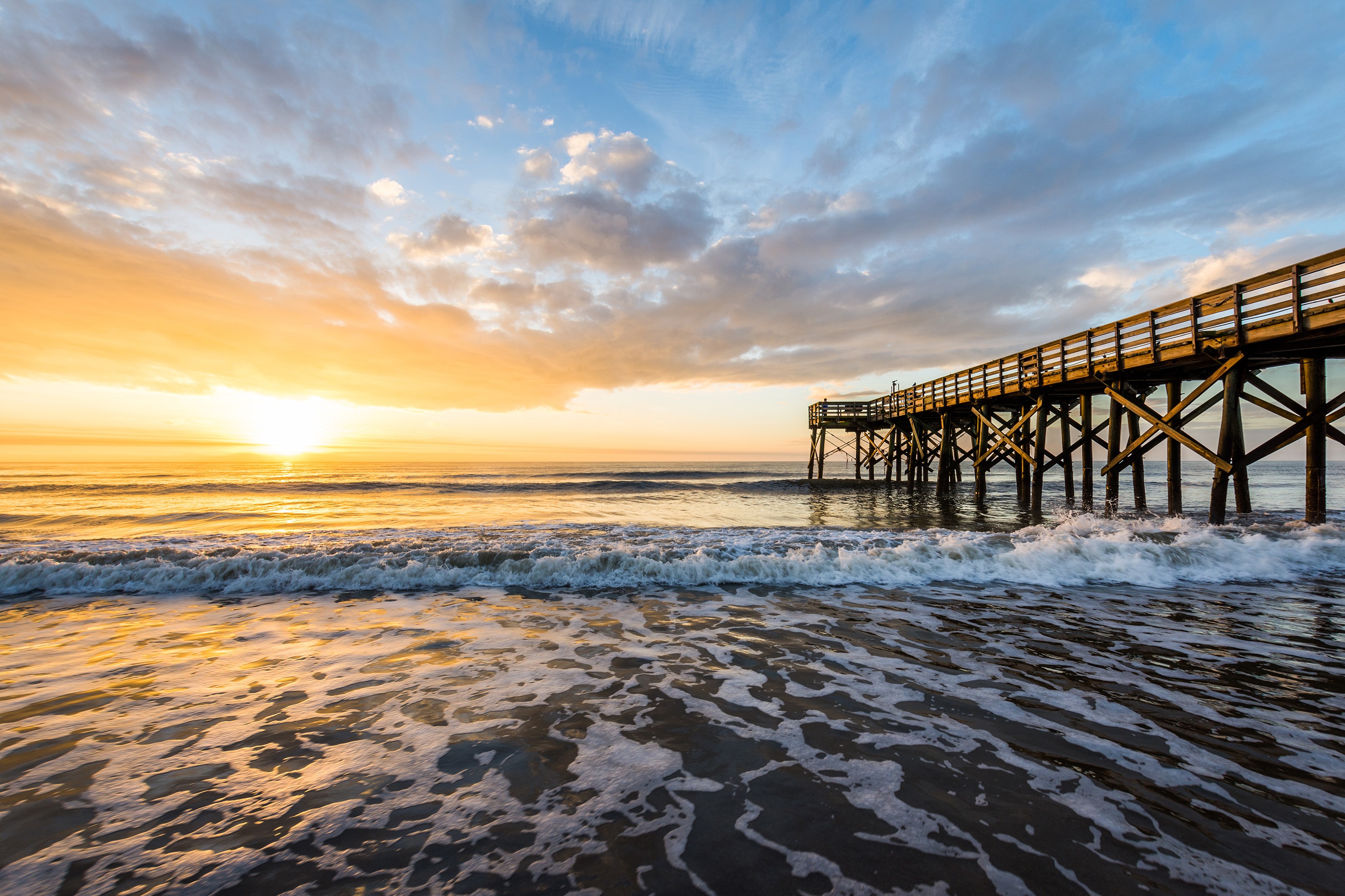 A wooden pier over South Carolina ocean waves at sunrise or sunset with a colorful sky.