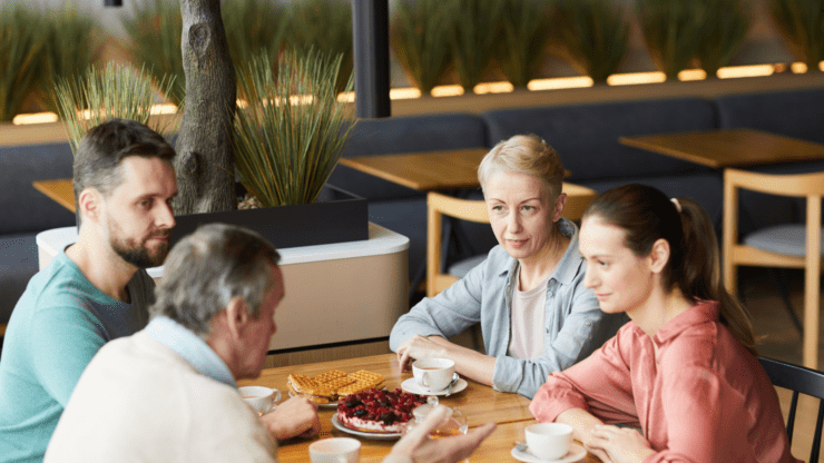 Family sits together at a table, drinking and eating while in conversation.
